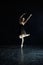 Ballerina in black dress in empty dark hall.