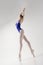 ballerina in a blue bodysuit and ballet shoes poses in a photo studio in motion showing beautiful long legs