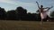 Ballerina dances on background of meadow, trees and blue sky.