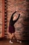 Ballerina in dark bodysuit, in dress in dark interior Studio. Wall of bricks, piano
