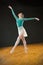 Ballerina in green leotard and skirt, dancing in the studio