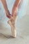 Ballerina hands puts pointe shoes on leg in dance class