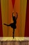 Ballerina silhouette of a young ballet lady dancing on pointe in attitude derriere position on stage in the spotlight with a red c