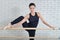 Ballerina stretches herself near barre at ballet studio, close up portrait of beautiful woman dancer looking at camera.