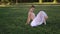 Ballerina in white dress sits on lawn and makes stretching exercises.