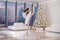 A ballerina in a white tutu poses in a bright hall with a Christmas tree