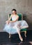 Ballet dancer ballerina in beautiful light blue dress tutu skirt posing sitting on vinage chair in loft studio