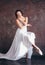 Ballet dancer ballerina in beautiful thin flying white dress is posing in dark loft studio