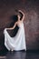 Ballet dancer ballerina in beautiful thin flying white dress is posing in dark loft studio