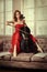 Ballet dancer in red dress and pointe playing on antique black cello