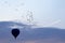 Balloons with people flying in the background of a flock of bird