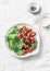 Balsamic marinated cherry tomato salad with pine nuts, spinach and grilled bread on a light background