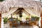 Bamboo benches with cushions, low round table are in an open thatched pavilion