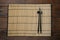 Bamboo mat with pair of black chopsticks and rest on wooden table, top view
