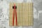 Bamboo mat with pair of red chopsticks and rest on grey textured table, top view