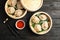 Bamboo steamers with tasty baozi dumplings, chopsticks and bowl of sauce on wooden background