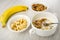Banana, bowl with muesli, bowl with slices of banana, spoon in bowl with granola, yogurt and banana on table