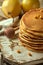 Banana pancakes stacked on a pale wooden platter, two pears in the backdrop, sea buckthorn berries and a honey spoon. An element