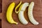 Banana, peeled banana and sliced banana on a wooden cutting board in top view