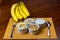 Banana sliced ramekin with oatmeal, granola and plain yogurt as side dishes under bamboo mat with bunch of bananas