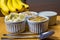 Banana sliced ramekin with oatmeal, granola and plain yogurt as side dishes under bamboo mat with bunch of bananas