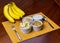 Banana sliced ramekin with oatmeal, granola and plain yogurt as side dishes under bamboo mat with bunch of bananas