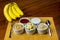 Banana sliced ramekin with oatmeal, granola, plain yogurt and honey as side dishes under bamboo mat with bunch of bananas