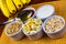 Banana sliced on ramekin and spoon pouring honey with oatmeal, granola, plain yogurt and honey as side dishes under bamboo mat