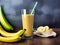 Banana smoothie in a tall crystal glass with banana fruits on a wooden surface