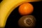 Banana, tangerine and kiwifruit on a black background