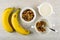 Bananas, bowl with muesli, pitcher with yogurt, spoon in bowl with granola on wooden table. Top view