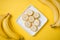 A banch of bananas and a sliced banana in a dish over yellow background.