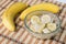 A banch of bananas and a sliced banana in a pot over a wood background