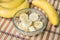 A banch of bananas and a sliced banana in a pot over a wood background