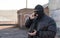 A bandit in a black leather jacket and a mask talking on the phone on the street near an abandoned building