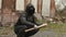 Bandit man in black mask and jacket with hood with baseball bat sits on street