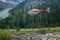 Banff, Canada - 08.30.2018: Red and blue Alpine helicopter going to touch down in a green meadow in Canadian Rockies. Service for