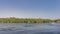 On the bank of a calm blue river there are dense thickets of green vegetation