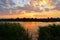 Bank of  river overgrown with tall dense grass in evening at sunset with clouds and pink, yellow, orange sky. Russian landscape