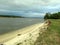 Bank of a wide river before a thunderstorm, yellow sand, dark water, wind, waves, dark clouds in the sky.