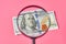 Banknote of one hundred dollars and magnifier on pink background