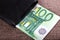 Banknotes of hundred euros sticking out of black wallet closed,