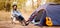 Banner format photo of young woman in warm sweater and black hat resting with guitar near camping tent in wilderness