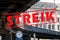 Banner with German text Streik meaning strike over an image with a clock under the curve of a suburban railway bridge in the