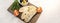 Banner with sliced bread on serving board served with olives, tomatoes, and fresh herbs on white table. Fresh, tasty option for