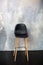 Bar stool stands against a gray concrete wall. Loft furniture design. Modern black chair standing in empty interior, cement wall d