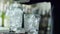 Bar worker holds metal scoop in arms and strew ice cubes into transparent glass close-up on desk