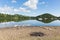 Barbecue ashes by beautiful lake on calm idyllic summer morning with cloud reflections