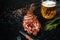 Barbecue dry aged rib of beef with spice, vegetables and a glass of light beer close-up on black wooden background