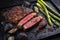 Barbecue dry aged wagyu rib-eye beef steaks with green asparagus and charred onions on a black cast iron design tray
